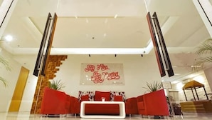A modern lobby with a red sofa set, a staircase, and a large wall with a red sign. - Tickle Hotel (Gondokusuman)