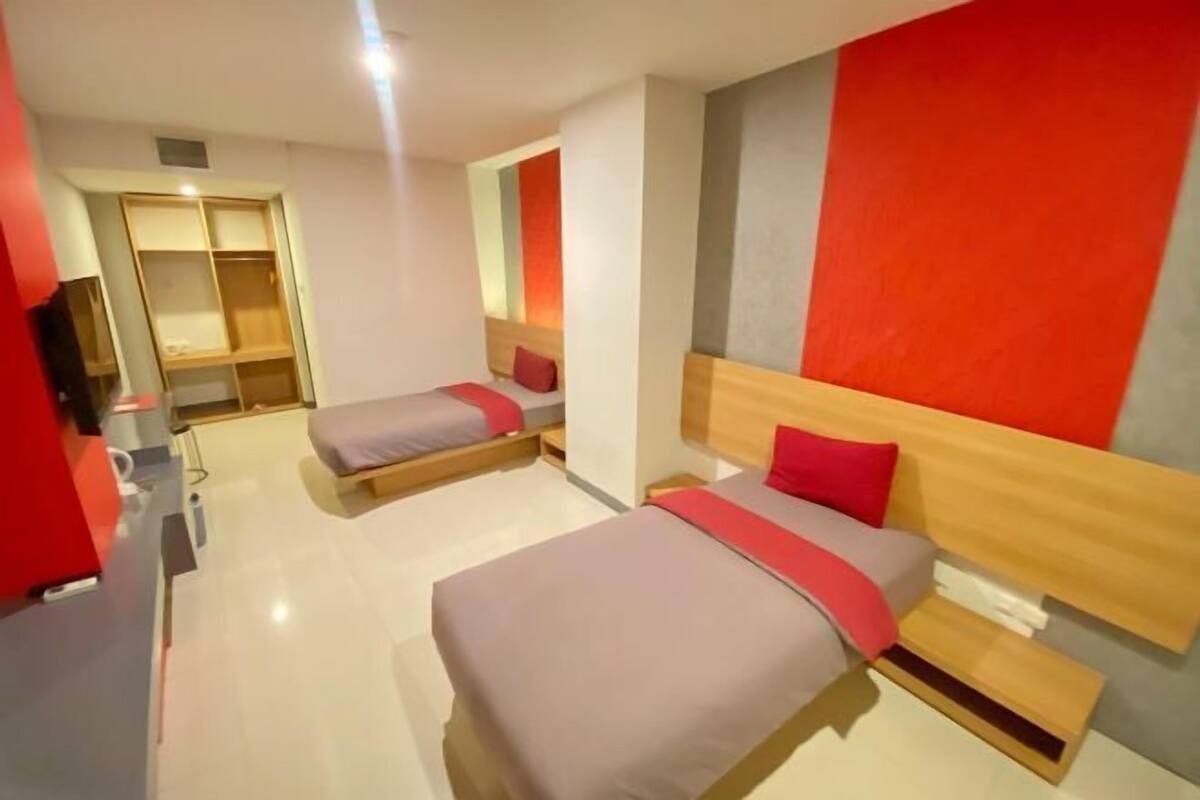 A hotel room with two beds, a wardrobe, a desk, and a television.
