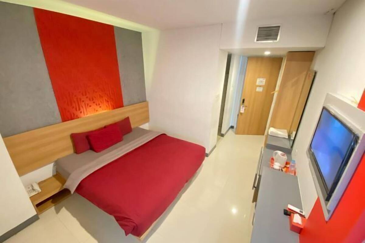 A hotel room with a bed, a TV, a desk, and a door leading to another room.