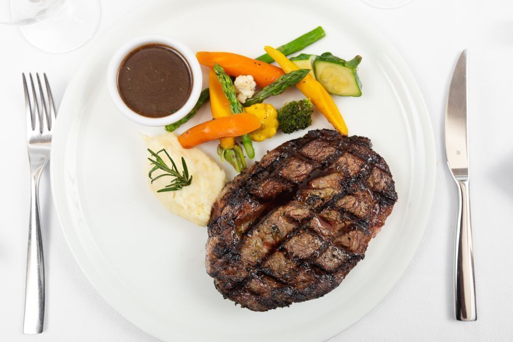 En tallerken med grillet steak, mos kartofler og en portion blandede grøntsager.