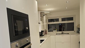 Una cocina moderna con armarios blancos, horno integrado, microondas y pileta doble.