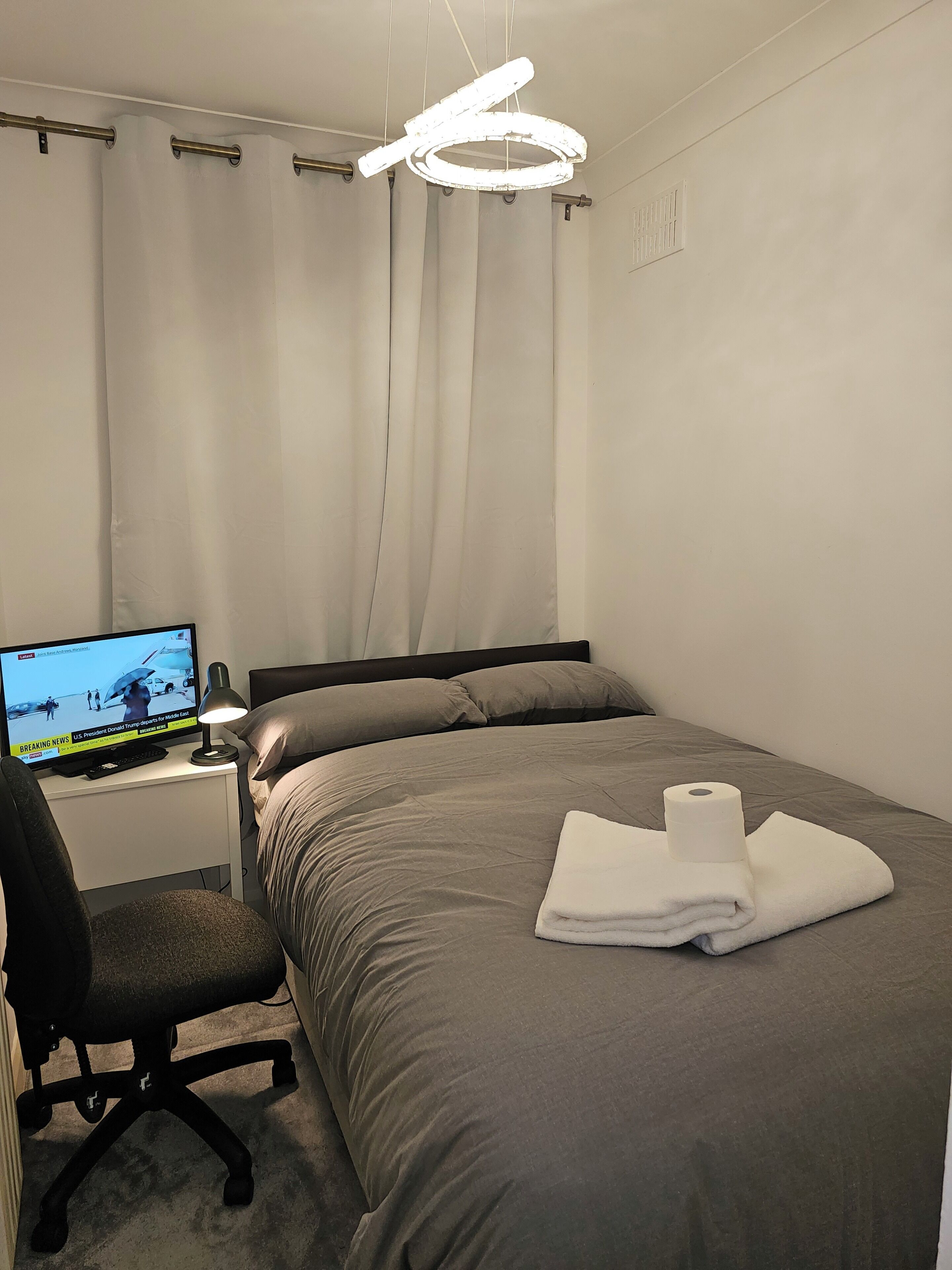 Een hotelkamer met een bed, een bureau met een computer, een stoel en een moderne lamp.