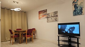 Una sala de estar con una mesa de comedor de madera, sillas rojas, un mueble bajo para televisión negro y obras de arte en las paredes.
