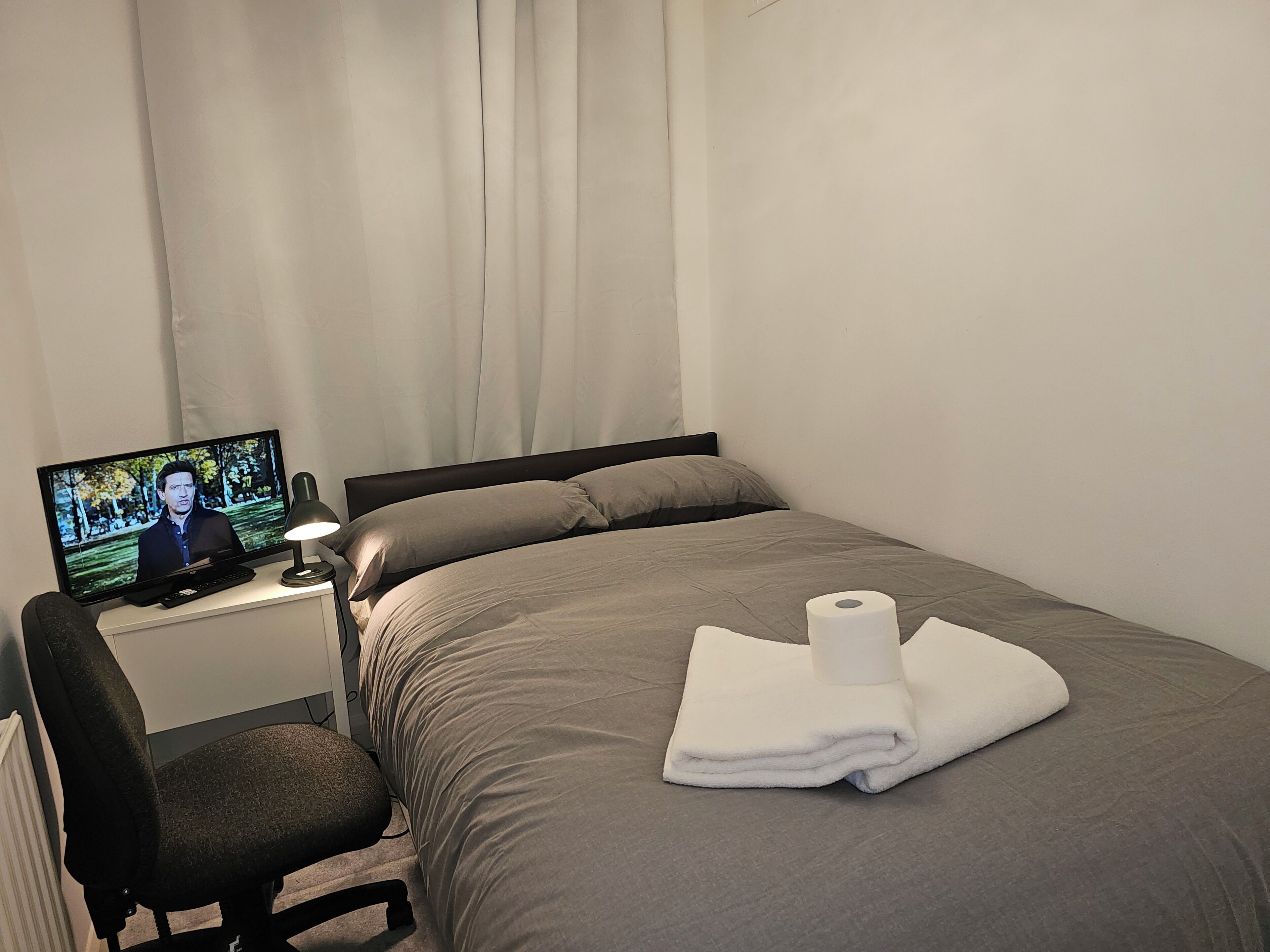 Ein Hotelzimmer mit einem Bett, einem Schreibtisch mit Computer, einem Sessel und einem Fenster mit Vorhängen.