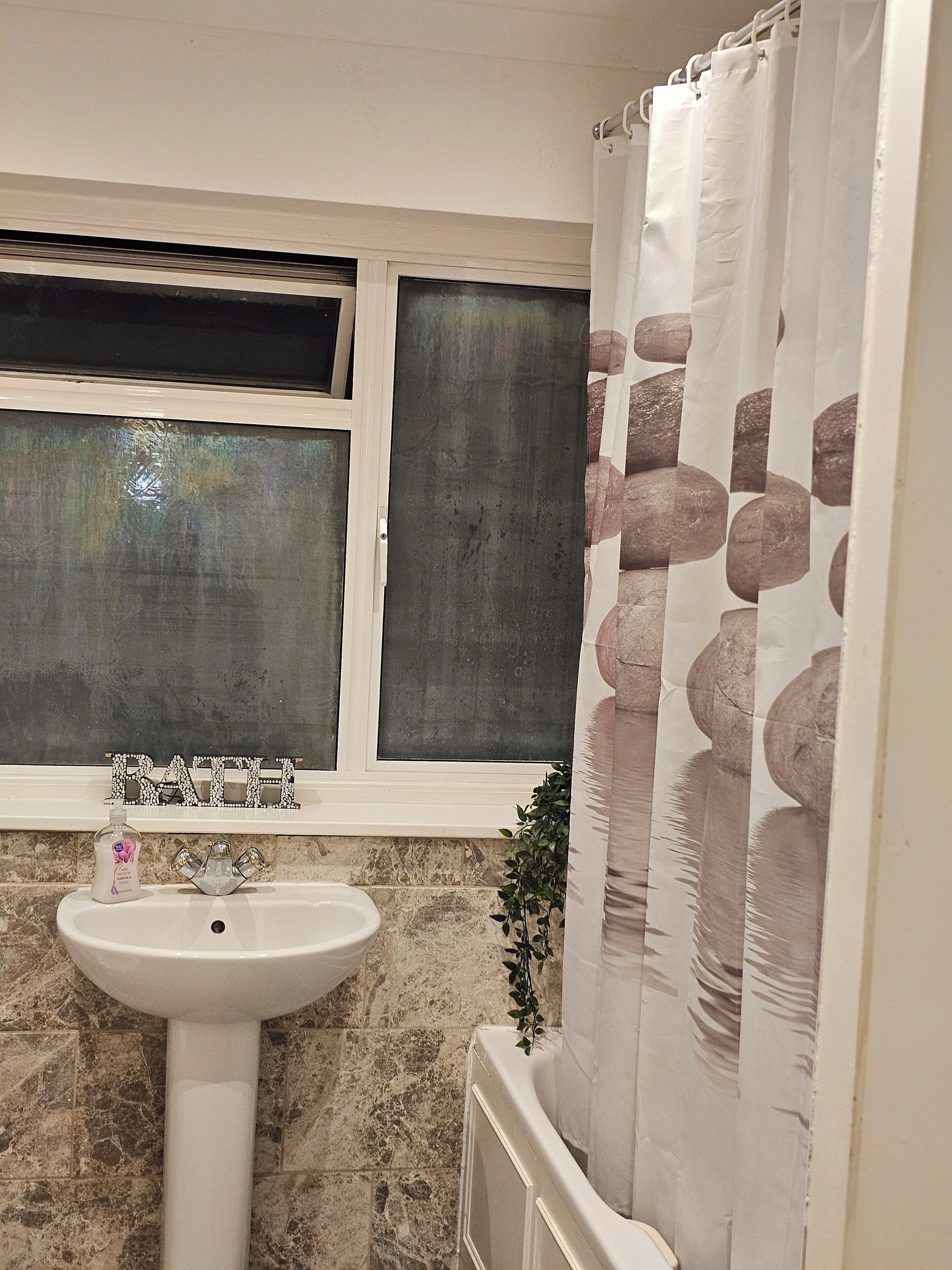 A bathroom with a sink, a window, and a shower curtain.