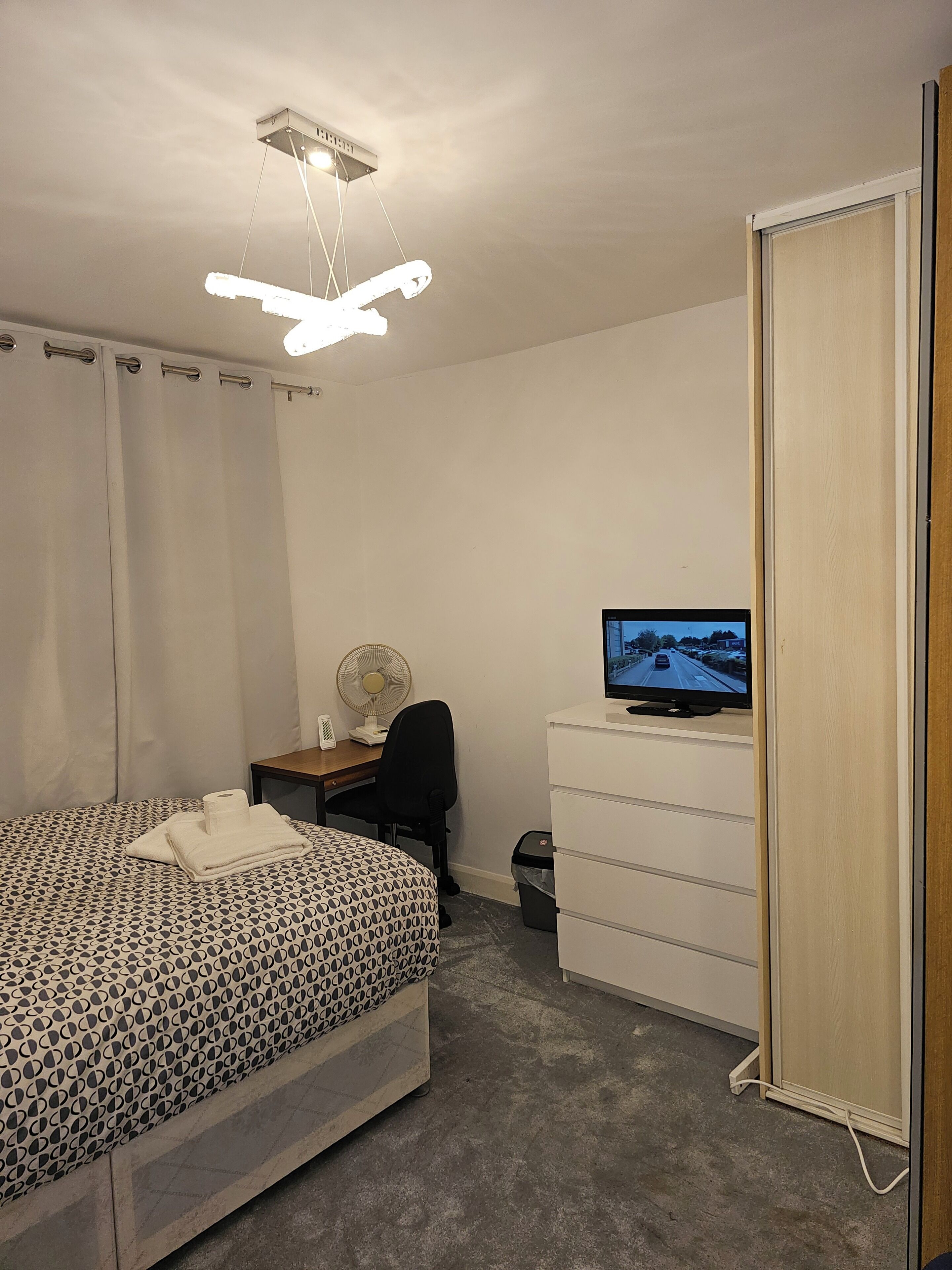 Une chambre à coucher comprenant un lit, un bureau, une chaise, une télévision, un ventilateur et une armoire.