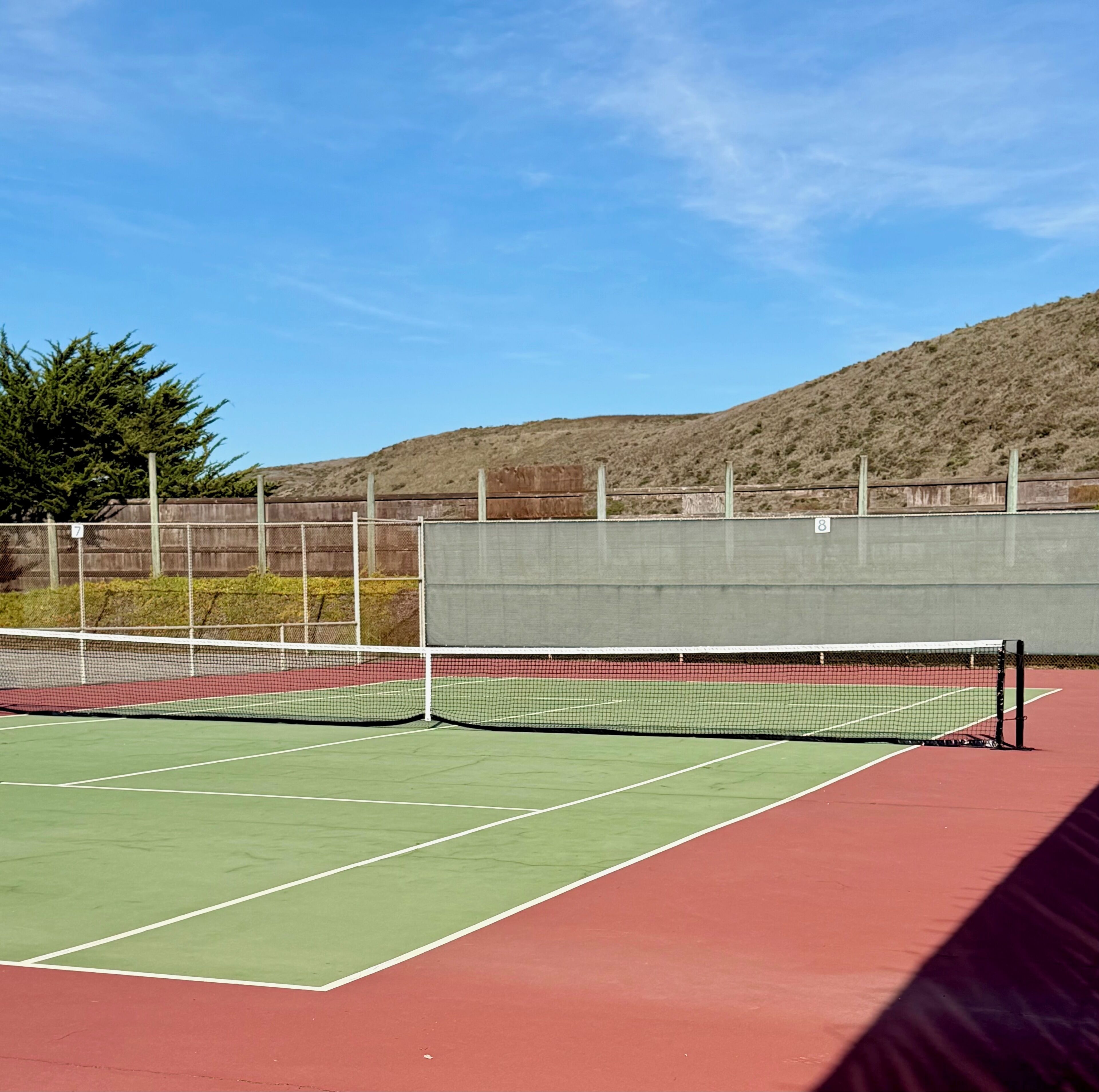 A tennis court with a net, green and red playing areas, and a fence with numbers 7 and 8.