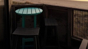 Terraza de madera con mesa y dos sillas frente a una playa al atardecer.