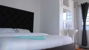 Een hotelkamer met een bed, een witte muur, een raam met gordijnen en een witte wastafel.