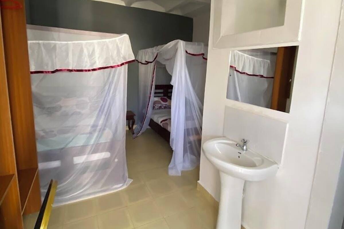 A bedroom with a bed under a canopy, a bedside table, and a window.