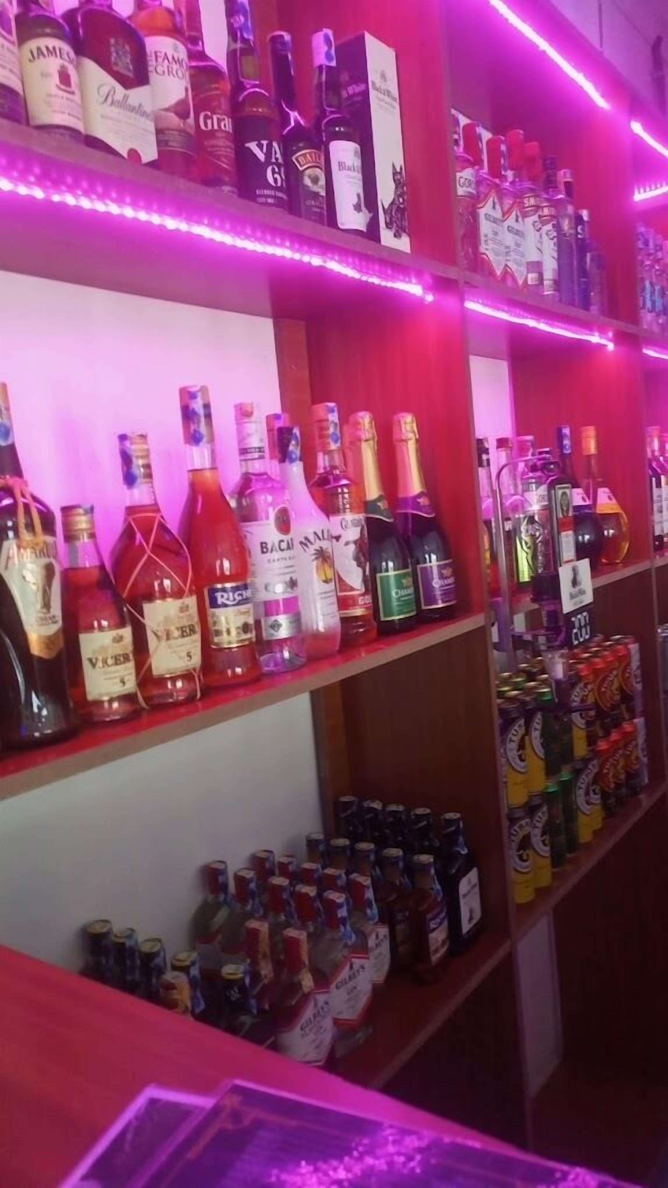 Shelves stocked with various liquor bottles and cans, illuminated by pink lighting.