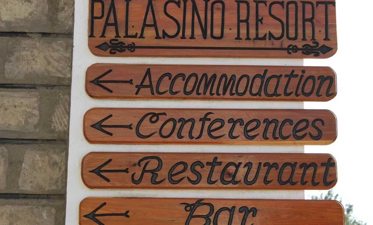 Un letrero de madera con flechas que indican las diferentes instalaciones del Palasino Resort, como Alojamiento, Conferencias, Restaurante y Bar.