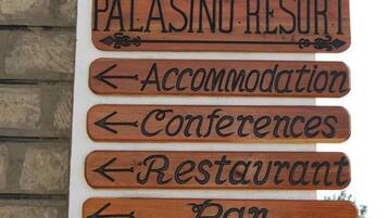 Un letrero de madera con flechas que indican las diferentes instalaciones del Palasino Resort, como Alojamiento, Conferencias, Restaurante y Bar.