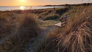 A coastal path with a wooden bench, leading to a beach with the sun setting in the background. - 5 Star Holiday Home in Hojby (Hojby)