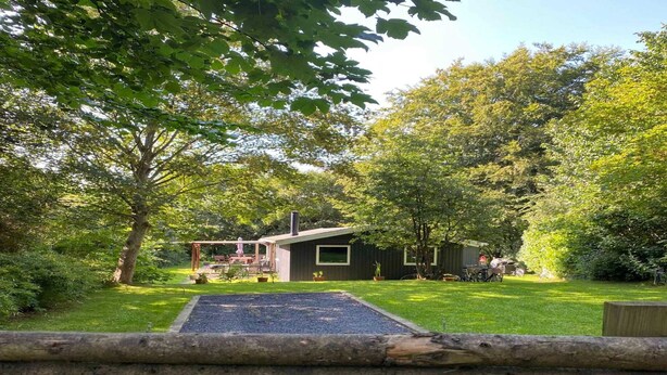 A rustic cabin with a deck, surrounded by lush greenery and a well-maintained lawn. - 5 Star Holiday Home in Hojby (Hojby)