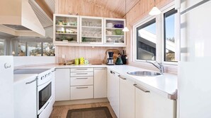 A modern kitchen with white cabinetry, a built-in oven, and a window providing natural light. - 5 Star Holiday Home in Pandrup (Pandrup)