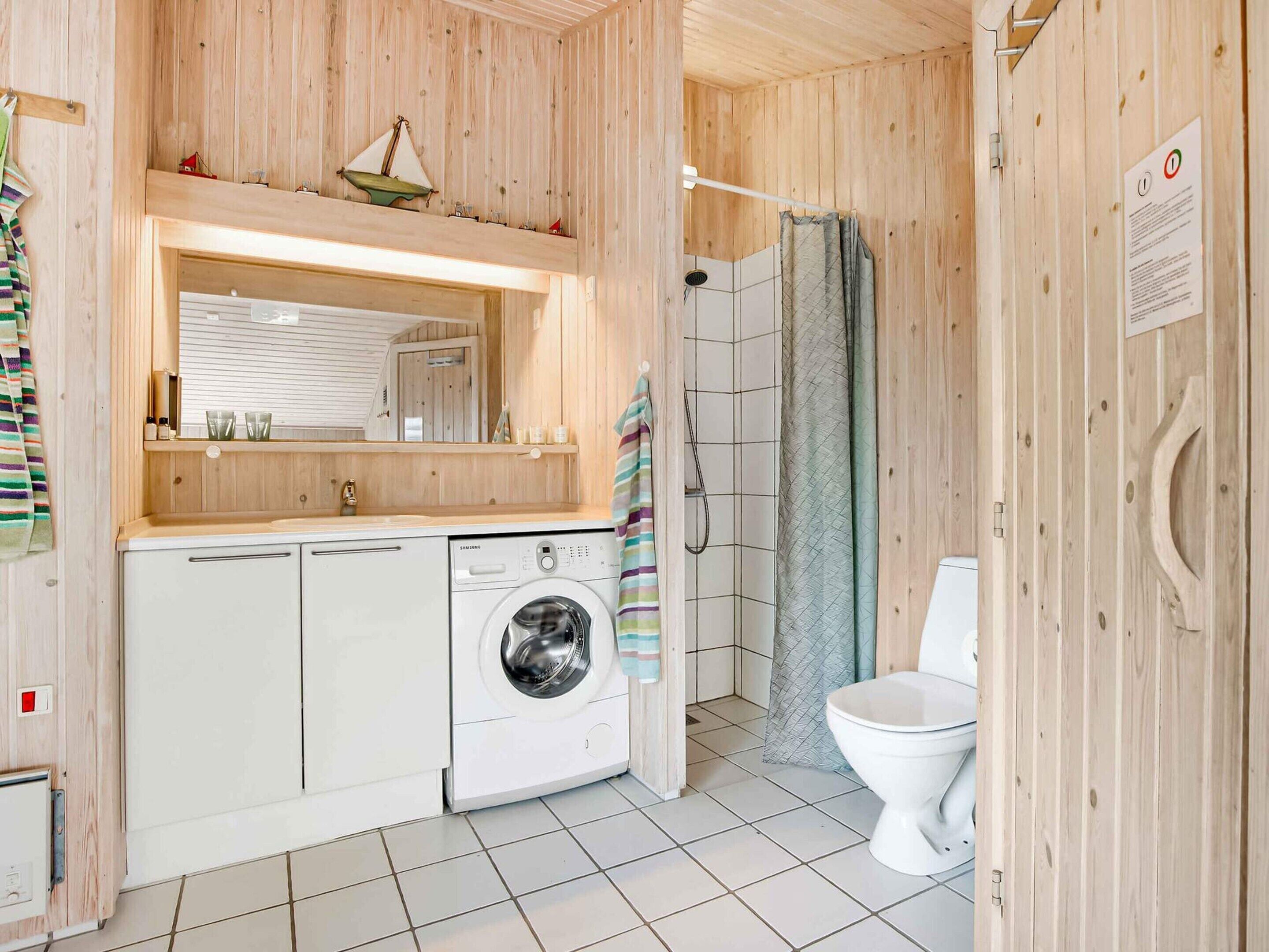 A compact, wooden-finished bathroom with a washing machine, toilet, and shower area.