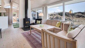 A modern living room with a built-in wood stove, large windows, and a cozy seating area. - 5 Star Holiday Home in Pandrup (Pandrup)