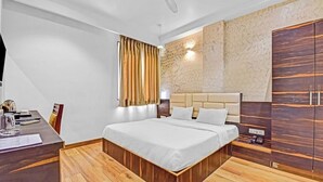 Une chambre d’hôtel moderne avec un grand lit, un plancher en bois, un bureau avec une chaise, une armoire et une fenêtre avec des rideaux.