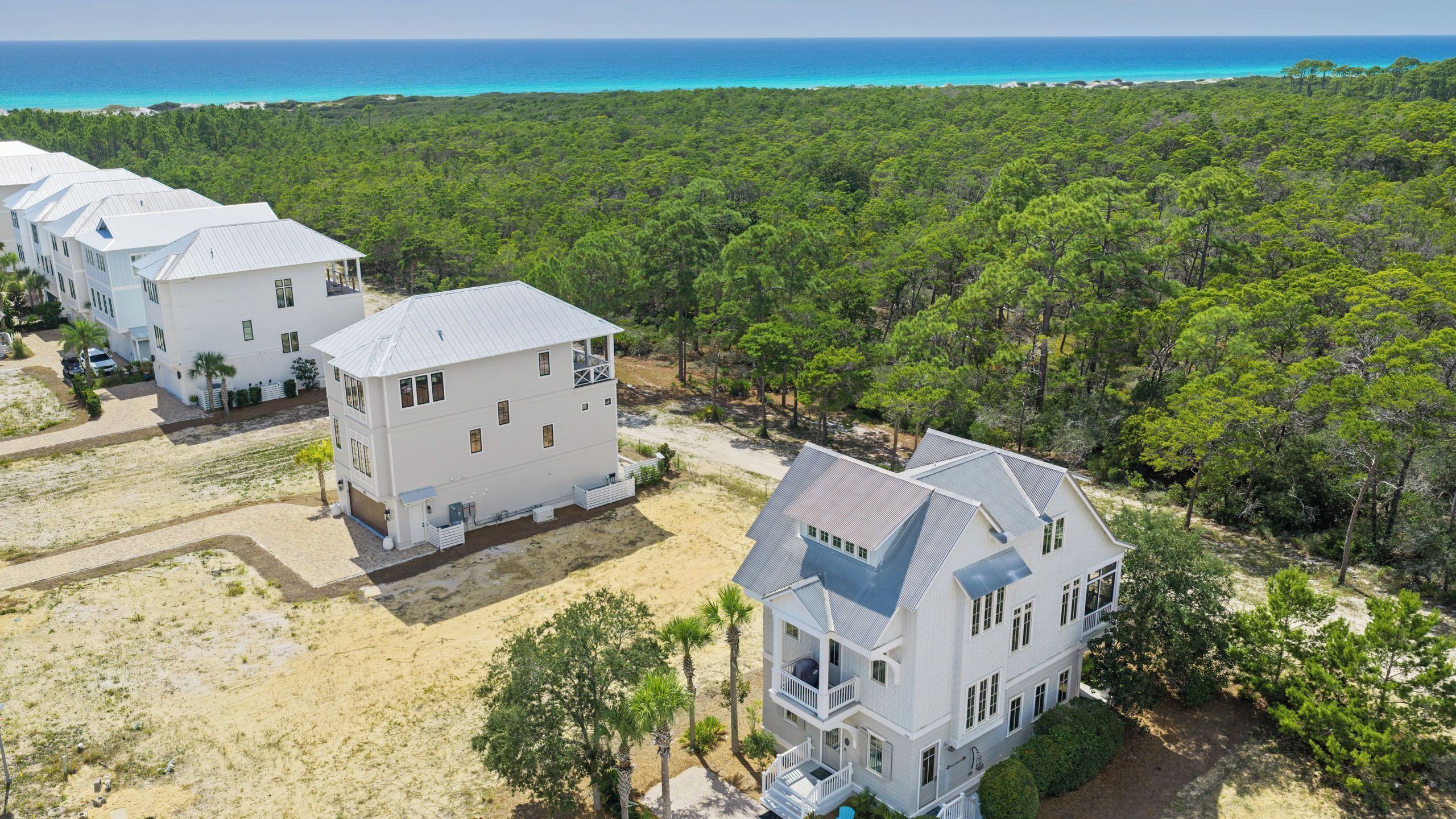 A coastal property with multiple white buildings, a sandy area, and dense green forest.