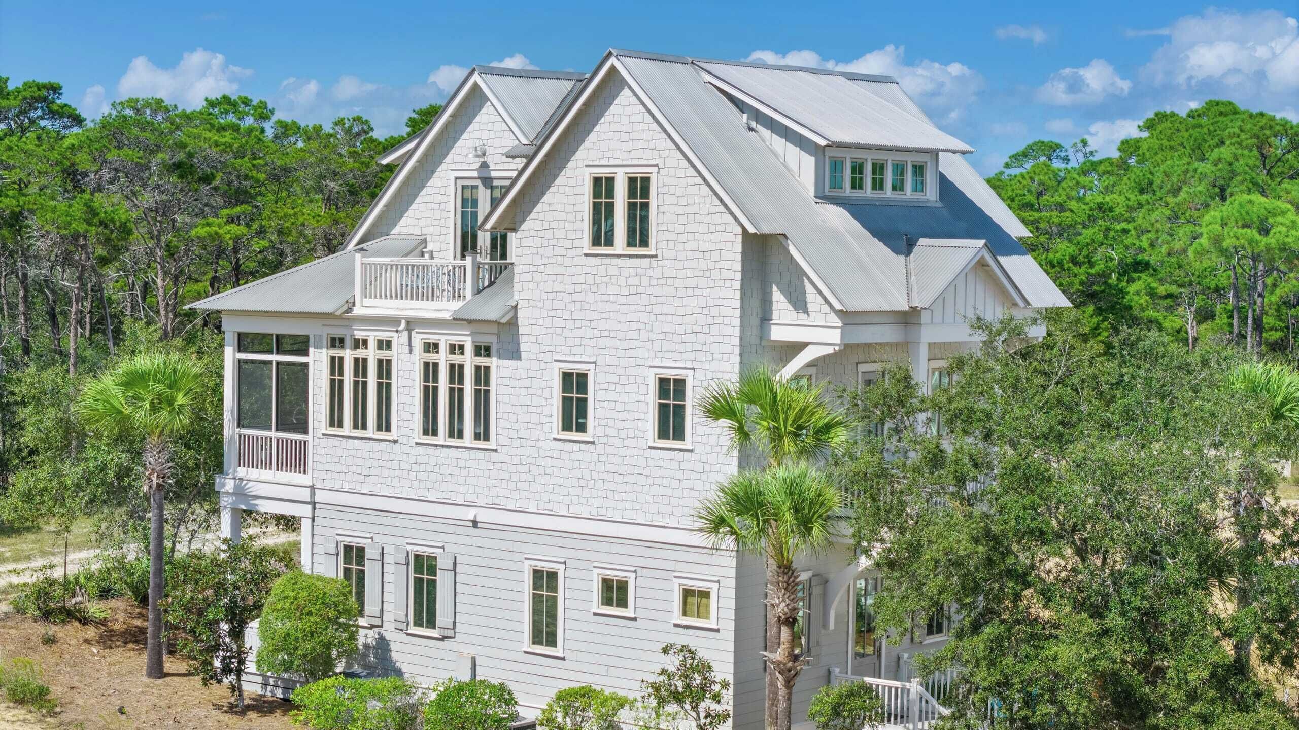 A large, two-story house with a balcony, surrounded by dense greenery and trees.