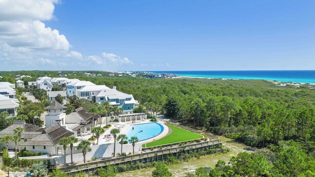 A resort with a large pool, lush greenery, and a view of the ocean.
