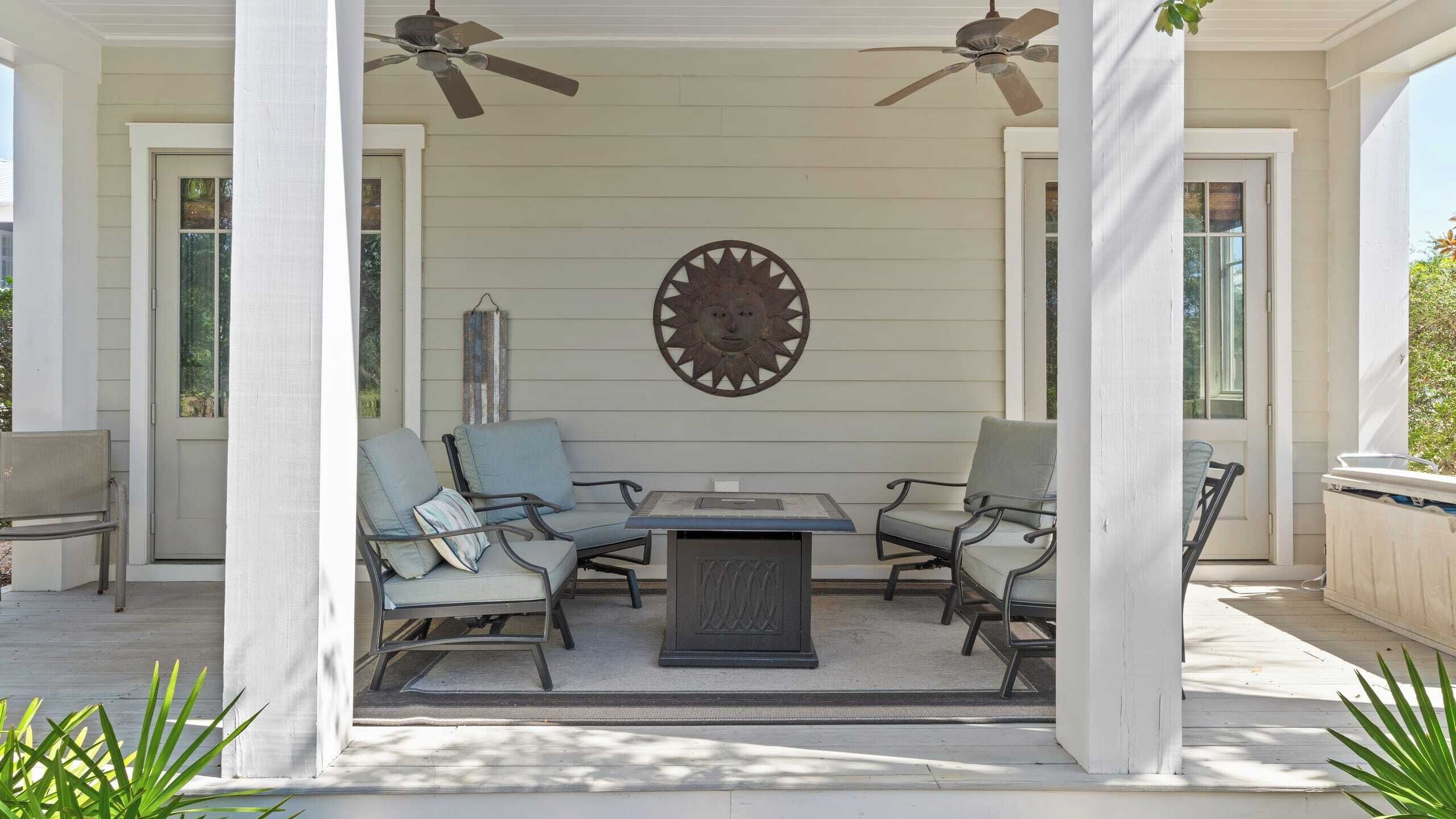 Een overdekt terras met een tafel en stoelen, plafondventilatoren en een decoratief wandpaneel.