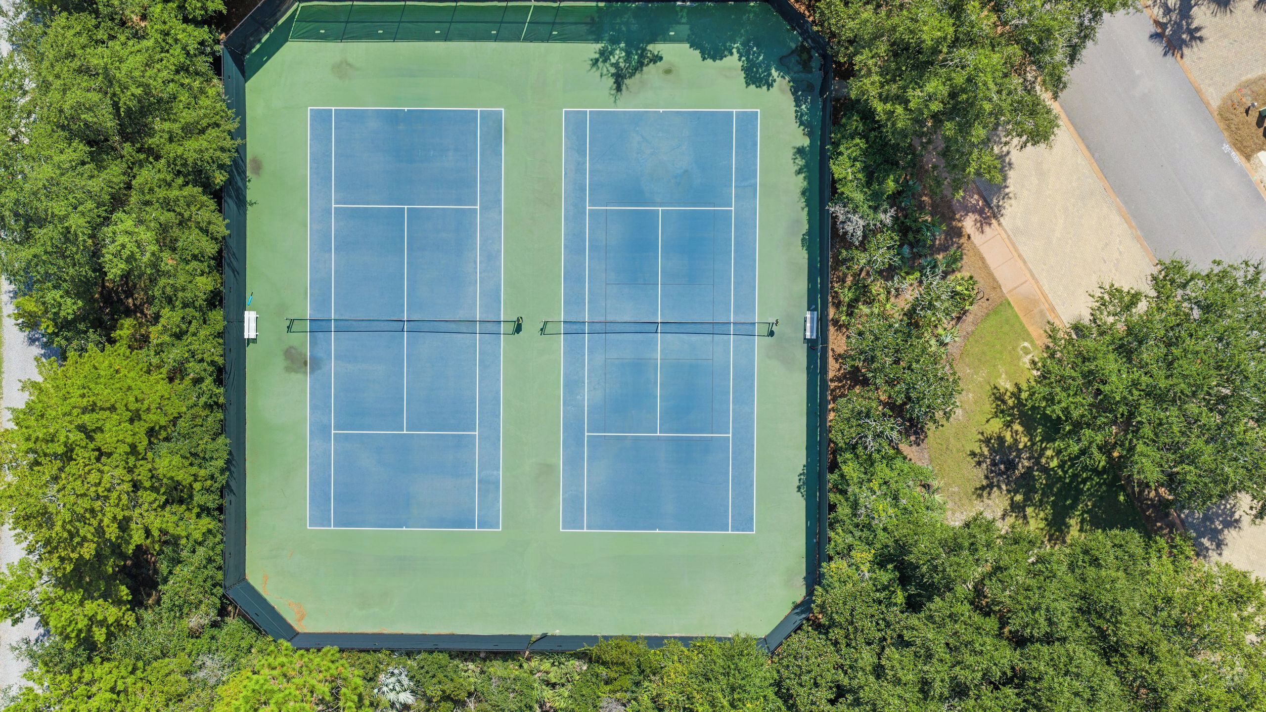 Vue aérienne d’un court de tennis entouré d’une végétation luxuriante.