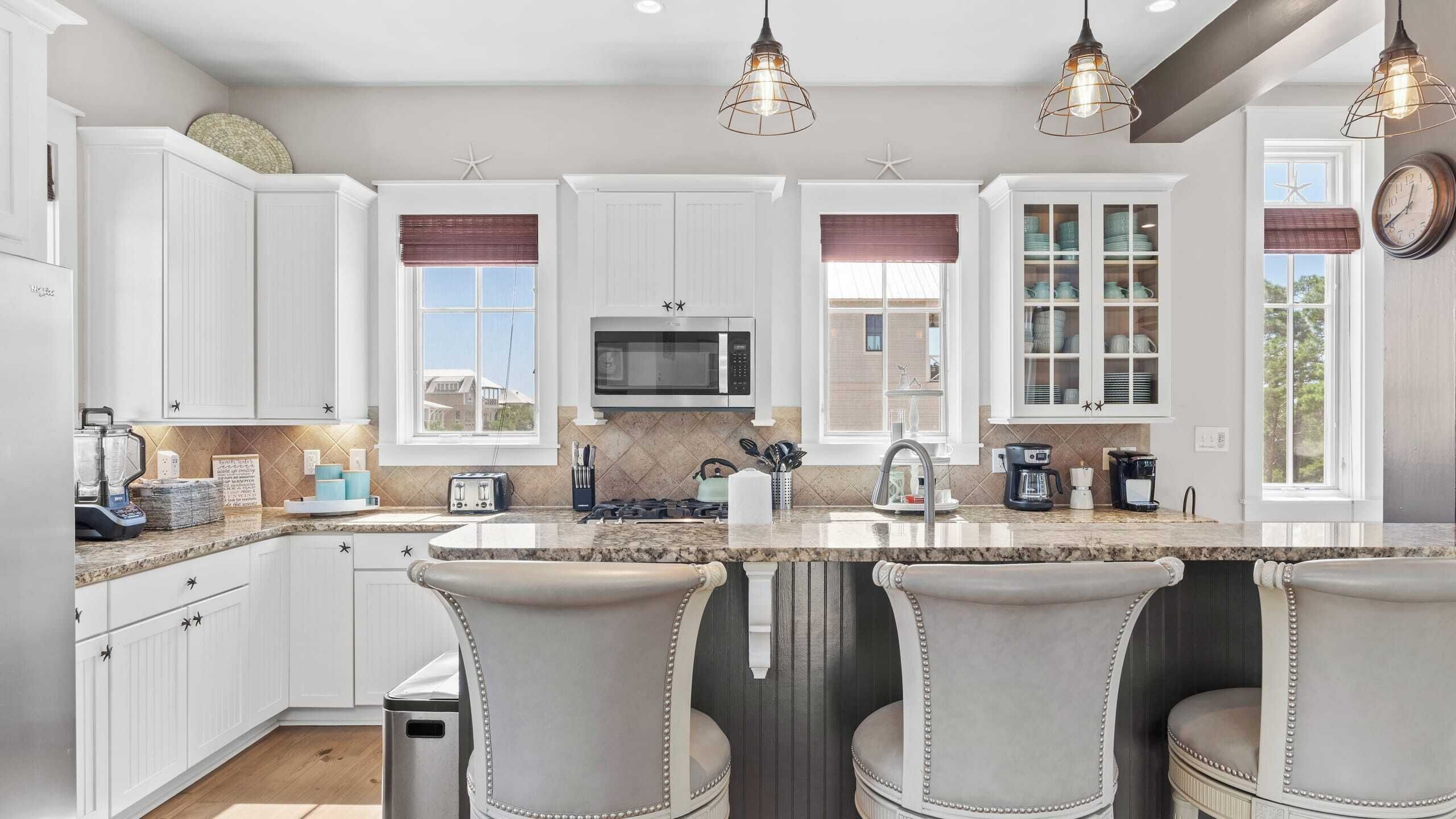 A modern kitchen with white cabinets, a central island with bar stools, a microwave, and a coffee station.