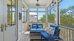 A covered porch with a blue sofa and a ceiling fan.