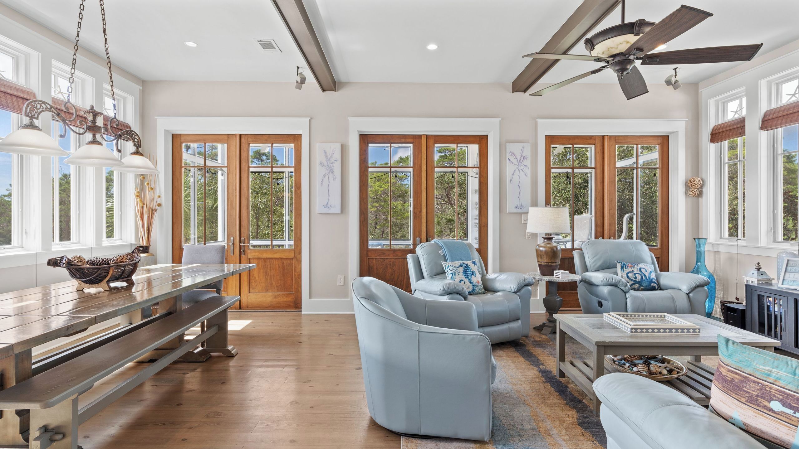 A spacious living room with a wooden bench, two grey armchairs, a coffee table, and a ceiling fan.