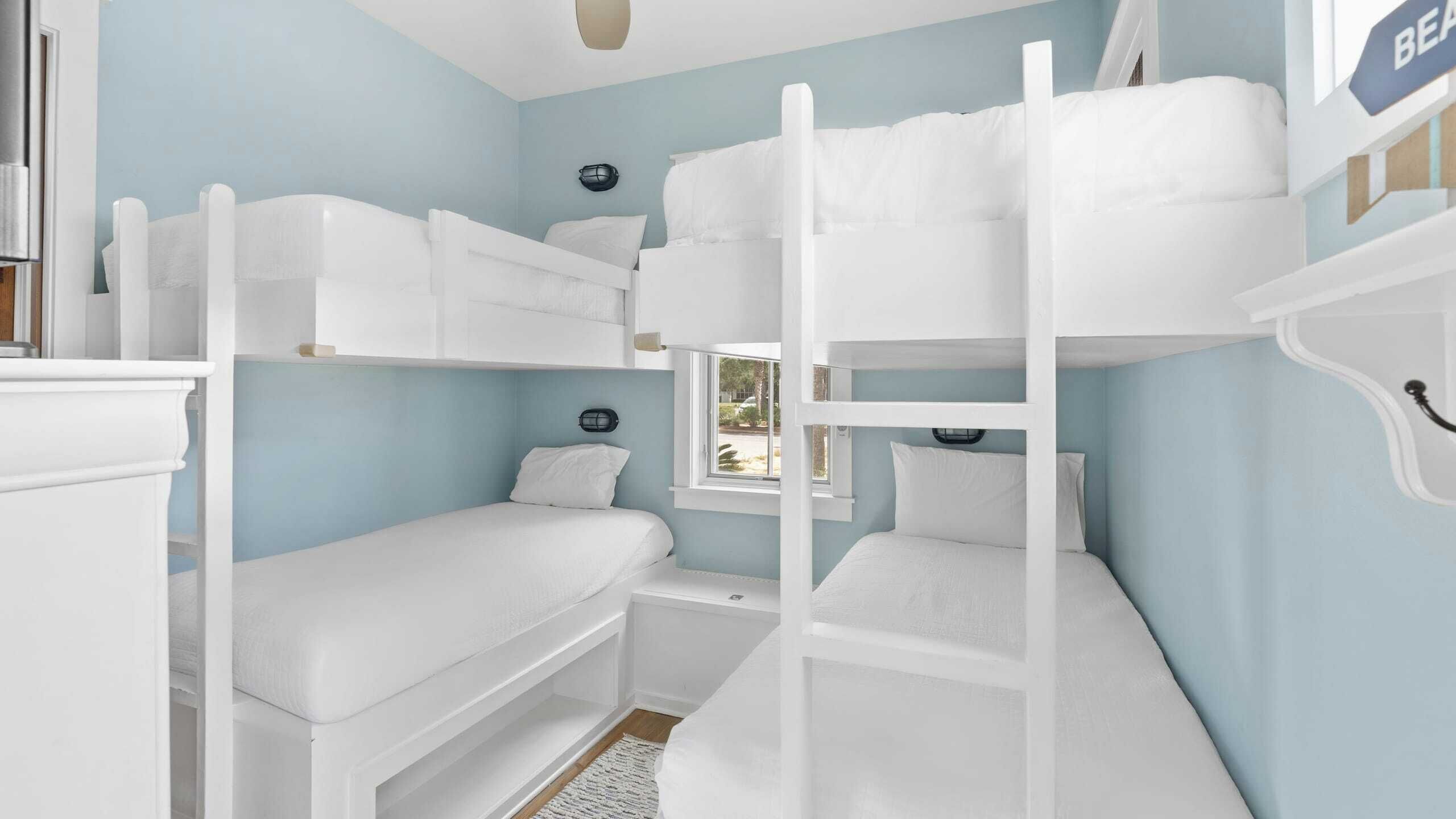 A bunk bed room with light blue walls, a window, and a bed with white bedding.