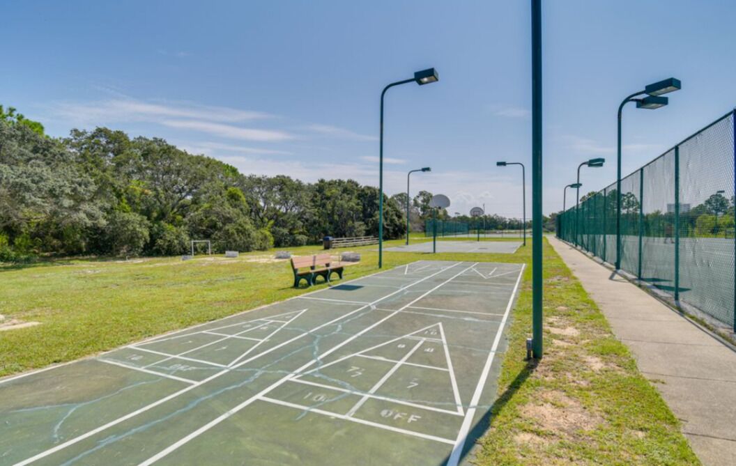 Un terrain de jeu extérieur vert, aménagé pour la pratique du shuffleboard, avec un banc et des lampadaires.