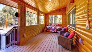 Eine Blockhütte mit einer Holzdachterrasse, einem Sofa mit Kissen und einem großen Fenster.