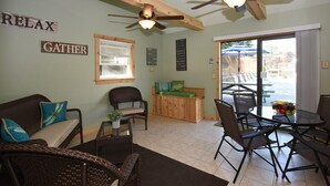 A cozy living area with a sofa, chairs, a coffee table, and a dining table with chairs. There is a ceiling fan, a window with blinds, and a view of the outside patio. - 1BR Villa Hideaway | Shuttle, Pools + Golf Nearby (Champion)