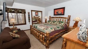 A bedroom with a rustic wooden bed, a brown sofa, a wooden nightstand, and a mirror. - 1BR Villa Hideaway | Shuttle, Pools + Golf Nearby (Champion)