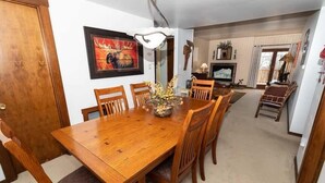 A dining area with a wooden table and chairs, a framed picture on the wall, and a fireplace in the background. - 1BR Villa Hideaway | Shuttle, Pools + Golf Nearby (Champion)