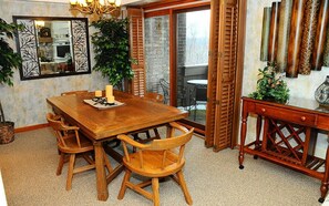 A dining area with a wooden table and chairs, a chandelier, and a view through a glass door to an outdoor patio. - Charming 2BR Villa | Cozy Stay w/ Pools + Shuttle (Champion)