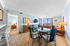 A spacious living area with a glass dining table, comfortable seating, and a view of the outdoors. - Romar Place 705 (Orange Beach)