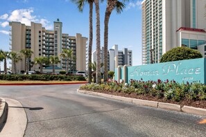 A hotel entrance with a sign reading 'Romar Place,' palm trees, and modern buildings in the background. - Romar Place 705 (Orange Beach)