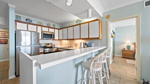 A kitchen with a central island, bar stools, and a refrigerator. - Romar Place 705 (Orange Beach)