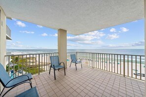 Een balkon met twee stoelen en uitzicht op het strand, onder een heldere lucht.