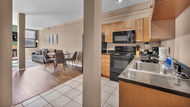A modern kitchen with wooden cabinets, a stainless steel sink, and a black stove. - 2-Story Townhouse in the Heart of Downtown (Cleveland)