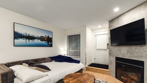 A modern living room with a sofa, a coffee table, a fireplace, a TV, and a large landscape painting on the wall. - Private Hot Tub | Pool | Free Parking | Sauna (Whistler)