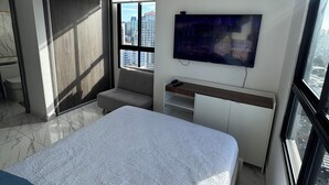 Een moderne slaapkamer met een groot bed, een aan de muur bevestigde televisie en uitzicht op de stad.