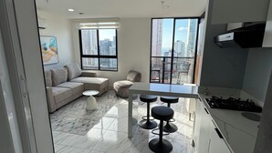 Een moderne keuken met een gasfornuis, een eethoek met barstoelen, een bank en een groot raam met uitzicht over de stad.