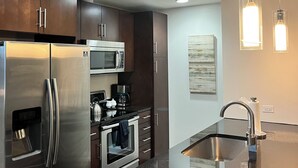 Une cuisine moderne dotée d’appareils électroménagers en acier inoxydable, de meubles de rangement en bois foncé et d’un éclairage suspendu.