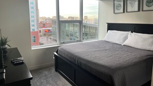 Une chambre avec une grande fenêtre, un lit, un bureau et une chaise.