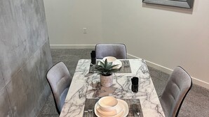 Un coin repas avec une table en marbre, quatre chaises, une plante en pot et un miroir encadré accroché au mur.