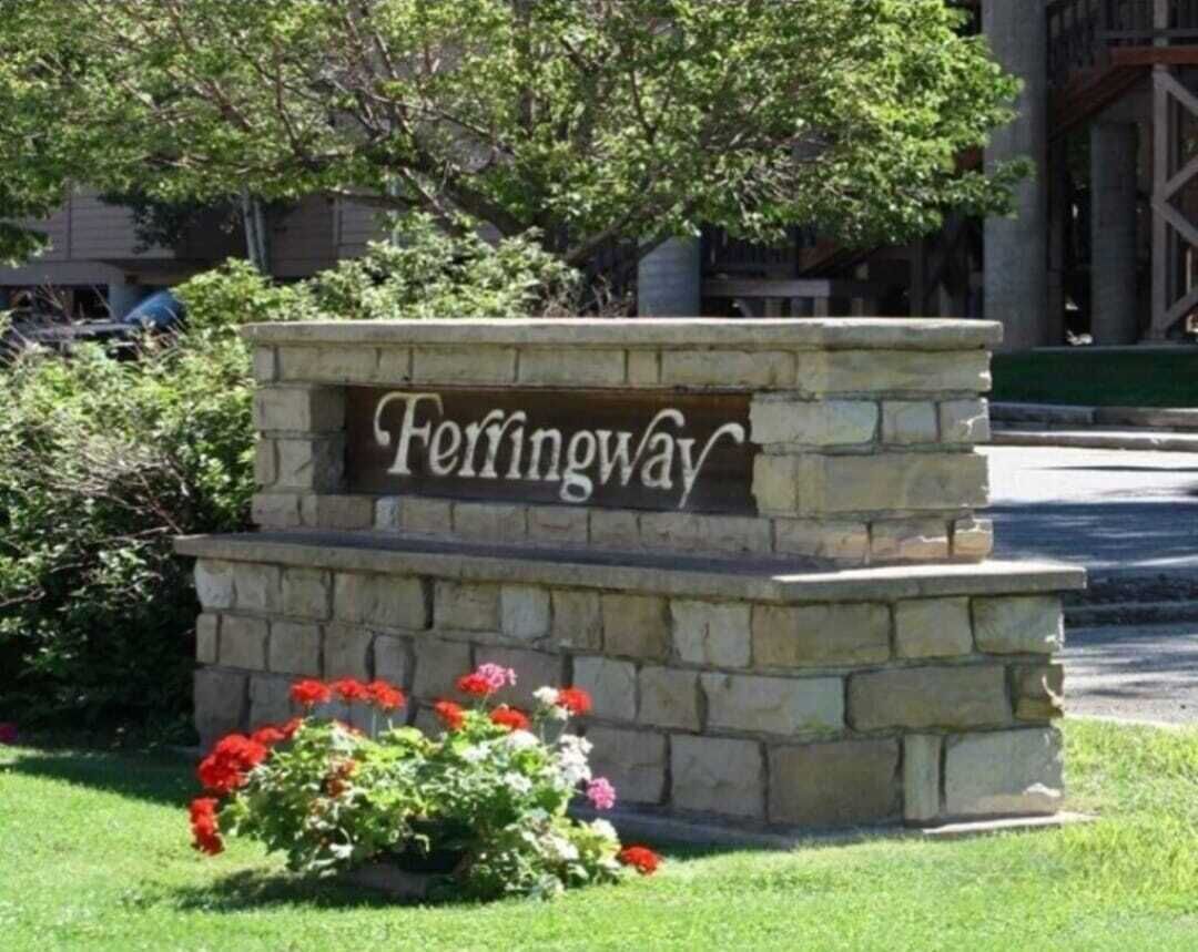 A stone sign with the name 'Ferringway' surrounded by a small garden with red flowers.